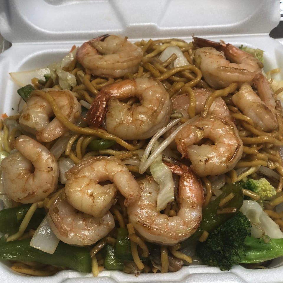 Shrimp lo mein with mixed vegetables, including broccoli, cabbage, and green peppers, in a white takeout container.